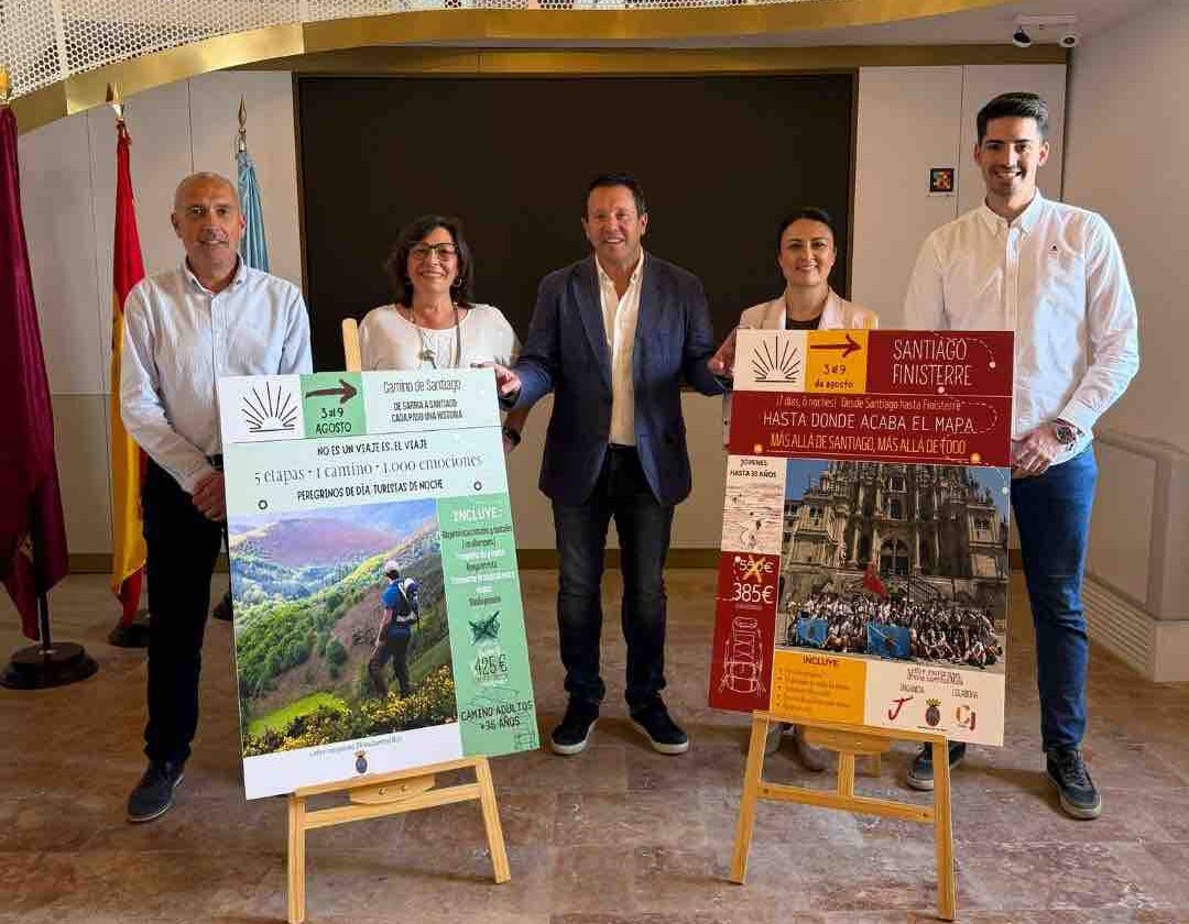 Five people pose behind two large Camino de Santiago travel posters on easels in a hall.