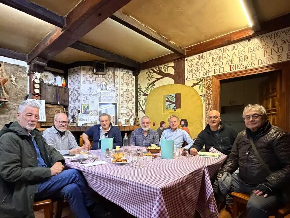Group of men sitting around a long table with a checkered tablecloth in a rustic restaurant, sharing a meal.