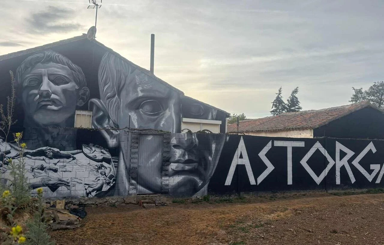 Black-and-white mural across a building wall featuring 2 llargs faces and the word ASTORGA in bold letters.
