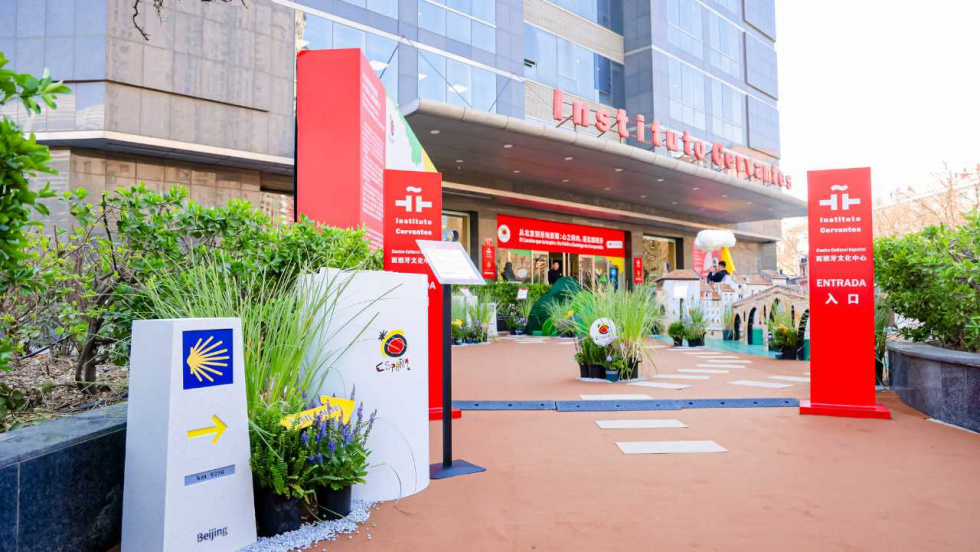 Pathway to a modern building entrance marked by red Institute Cervantes signage and surrounding potted plants