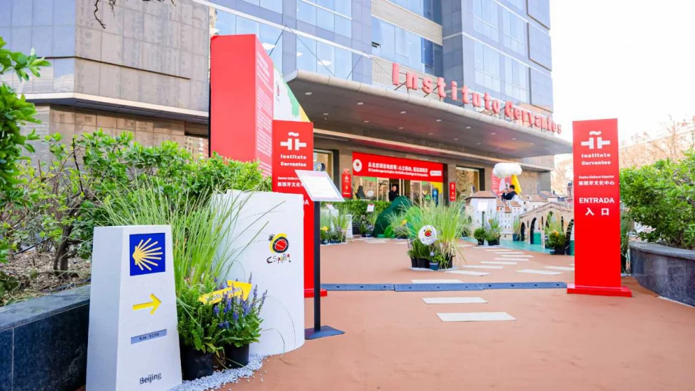 Pathway to a modern building entrance marked by red Institute Cervantes signage and surrounding potted plants