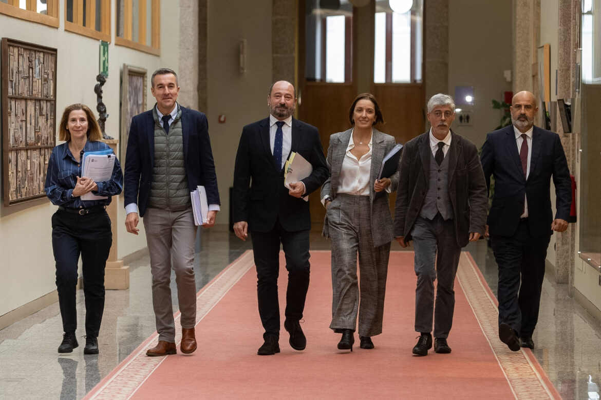 Six professionals walking down a hallway together, carrying folders and documents, in formal attire.