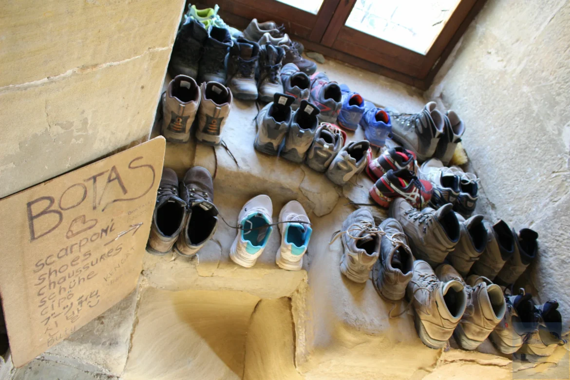 Multiple pairs of shoes arranged along a stone stairwell next to a window.