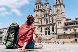 Two travelers with backpacks sit on a sunlit stone plaza, facing a grand historic cathedral in an urban square.