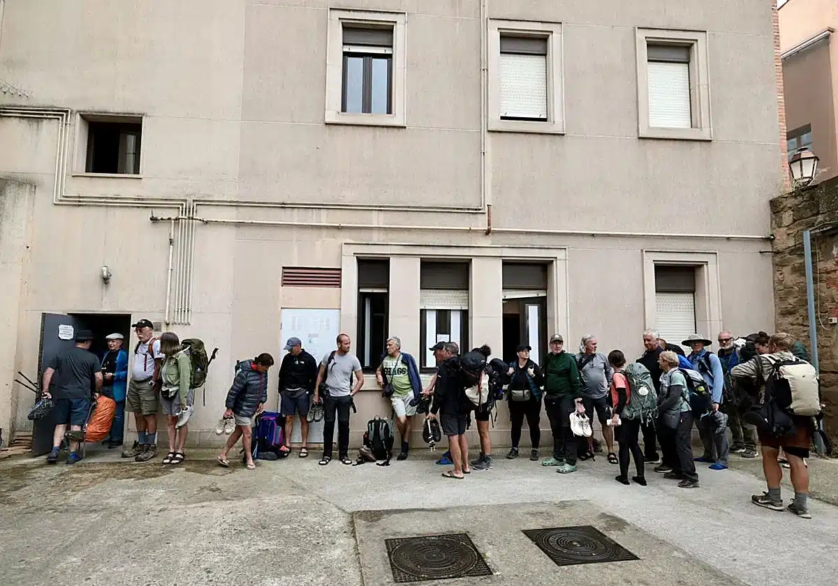 Line of hikers with backpacks waiting outside a beige building, ready for a tour.