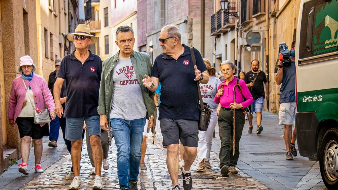 Group of adults walking along a narrow cobblestone street in a historic town, chatting and map-free, with a bus parked on the side behind them.