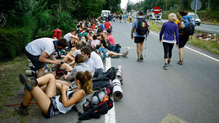 Group of hikers resting on the roadside with backpacks and rolled sleeping mats during a long walk event.