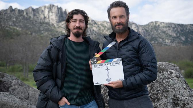 Two men in jackets stand outdoors on a rocky hillside; one holds a clapperboard reading 'Diario de un Mago'.