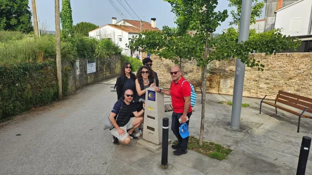 Group of five adults posing around a small public fountain on a sunny village street.
