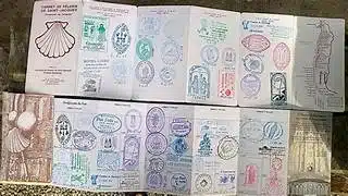Pasaporte estiloko liburuxka irekia zigilu-itxurako ilustrazio koloretsuz betea, gainazal batean laua.