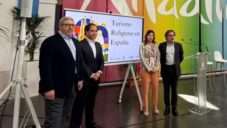 Four people stand on a stage beside a screen reading 'Turismo Religioso en España,' with a colorful mural backdrop.