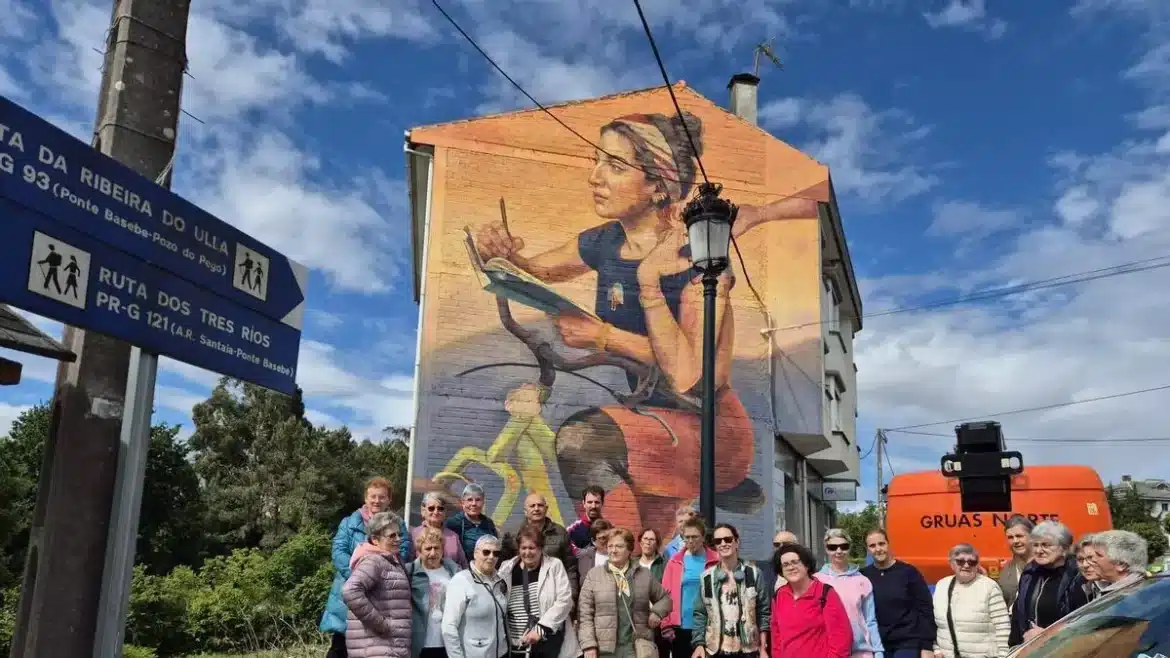 Group of seniors posing in front of a large mural of a girl reading on the side of a building, with a blue street sign and an orange truck nearby.