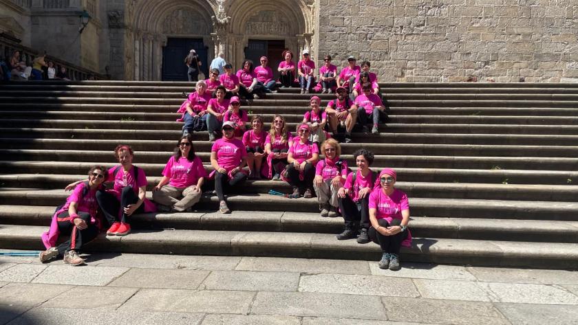Group of people in pink shirts posing on wide stone steps outside a historic building with arched entrance.