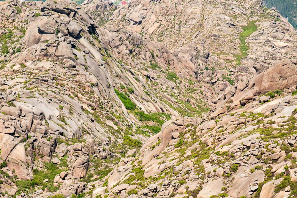 Rugged mountain terrain with large granite boulders and sparse green shrubs nearby.