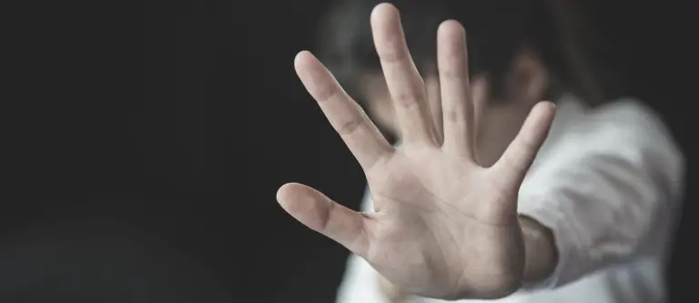 Outstretched hand signaling stop or asking for distance, with a dark background behind it.