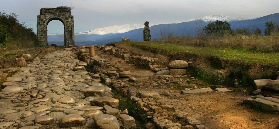 Stone archway and ancient ruins along a rocky path with snow-capped mountains in the background.