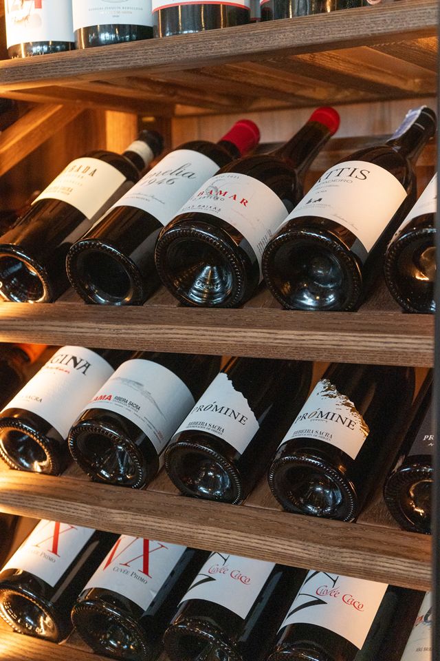 Row of wine bottles lying on wooden shelves in a wine shop display.