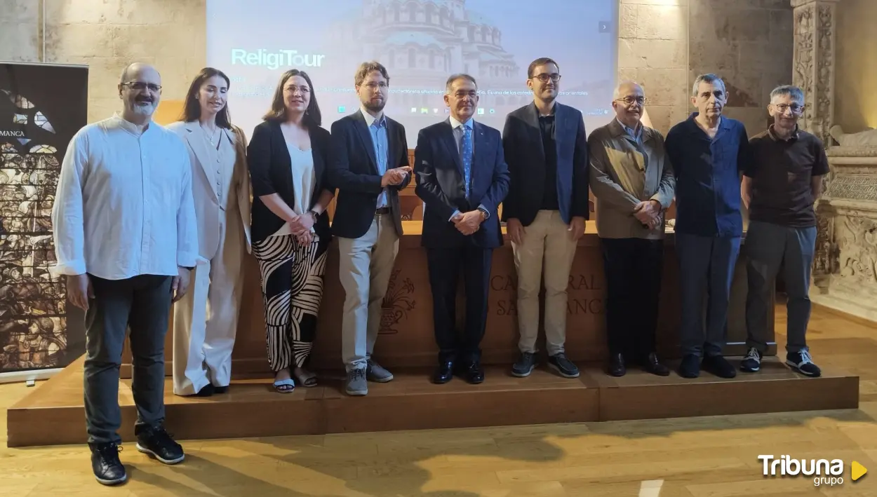 Group of eleven people standing on a wooden stage in a conference room, posing for a photo with a projection screen behind them showing 'ReligiTour' and a historic backdrop. Tribuna Grupo logo at bottom right.