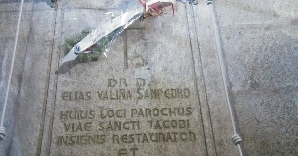 Stone gravestone with a Latin inscription and a small flower bouquet tied with a red ribbon laid across it.