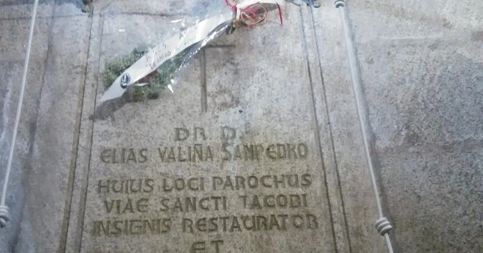 Stone gravestone with a Latin inscription and a small flower bouquet tied with a red ribbon laid across it.