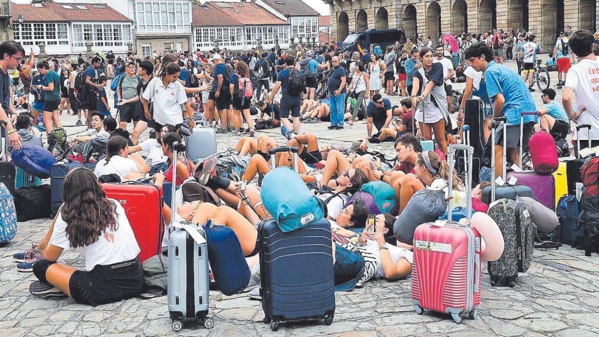 Crowd of travelers sitting among suitcases and backpacks in a busy square.