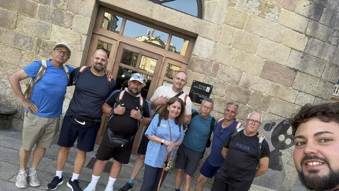 Group of hikers posing for a photo in front of a gray stone building entrance, wearing backpacks and athletic clothing.