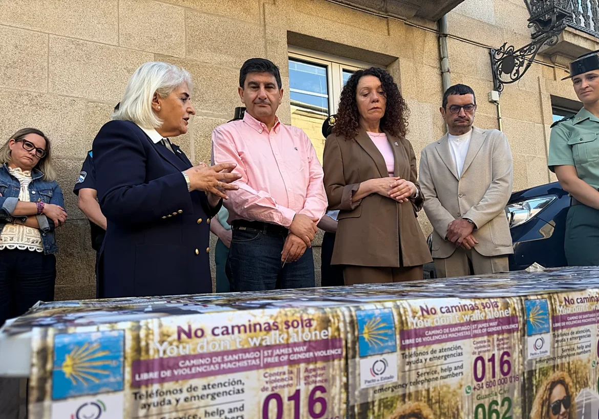 Group of adults standing outside a building at a campaign event about preventing gender-based violence, with a table covered in 'No caminas sola' posters in the foreground.