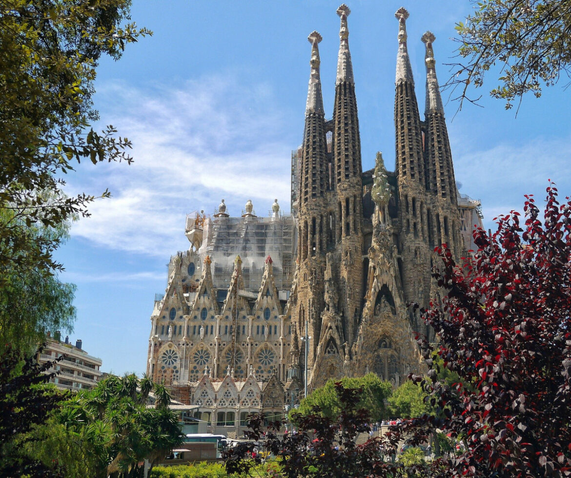 Sagrada Família basilica in Barcelona with tall spires against a blue sky and surrounding greenery.