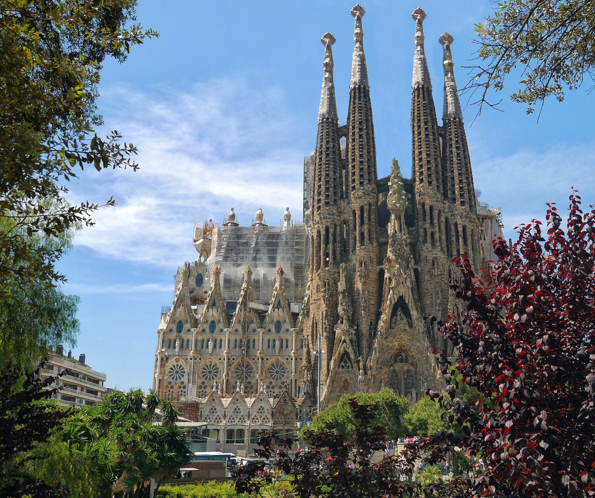 Sagrada Família basilica in Barcelona with tall spires against a blue sky and surrounding greenery.