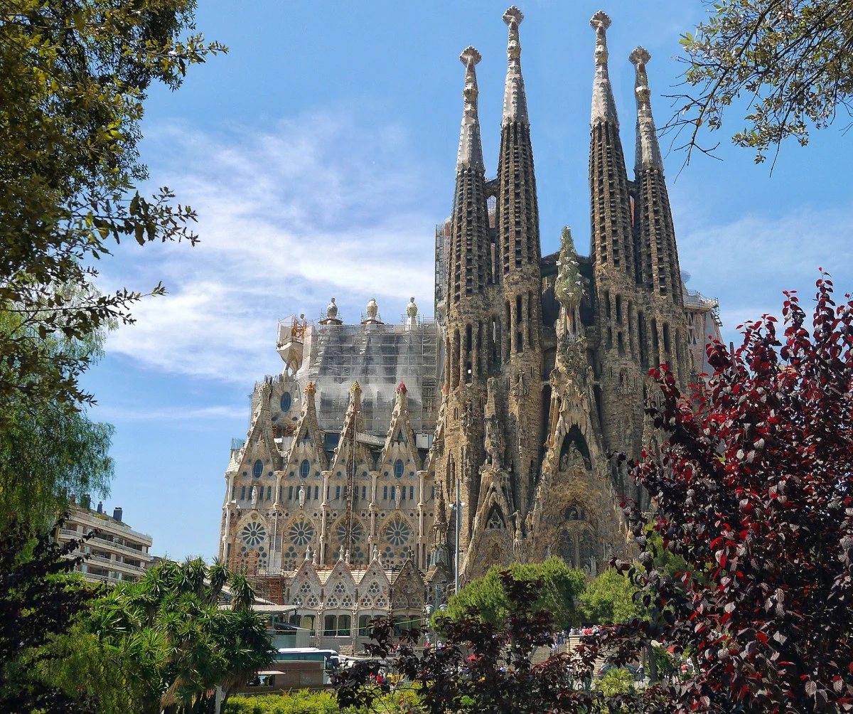 Basilique de la Sagrada Família à Barcelone avec de hautes flèches sur un ciel bleu et une verdure environnante.