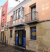Narrow cobblestone street lined with pastel-colored buildings; a storefront with a blue door and a wrought-iron balcony above.