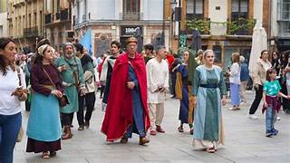 People in colorful medieval costumes walk through a town square during a street festival parade.