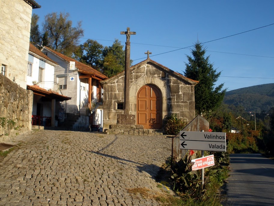 Small stone church with wooden door and two crosses on the roof, in a cobblestone village square.