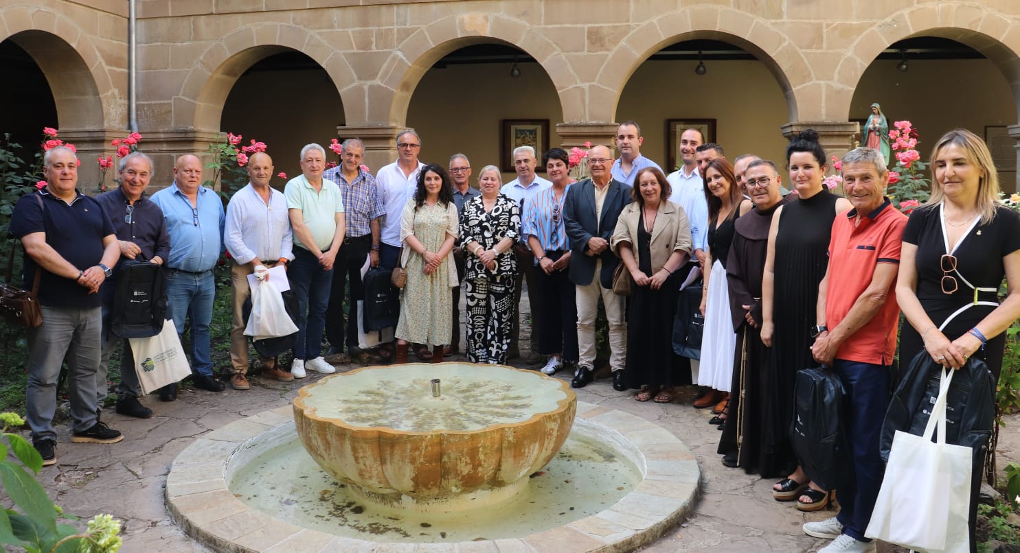 Group of adults posing around a circular fountain in a stone courtyard with arches and pink roses nearby.