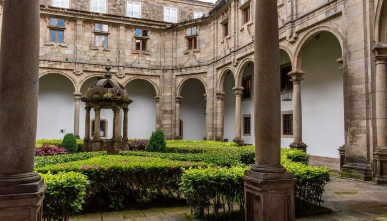 Stone cloister courtyard with arches and columns, a domed central fountain, and trimmed hedges around the garden.