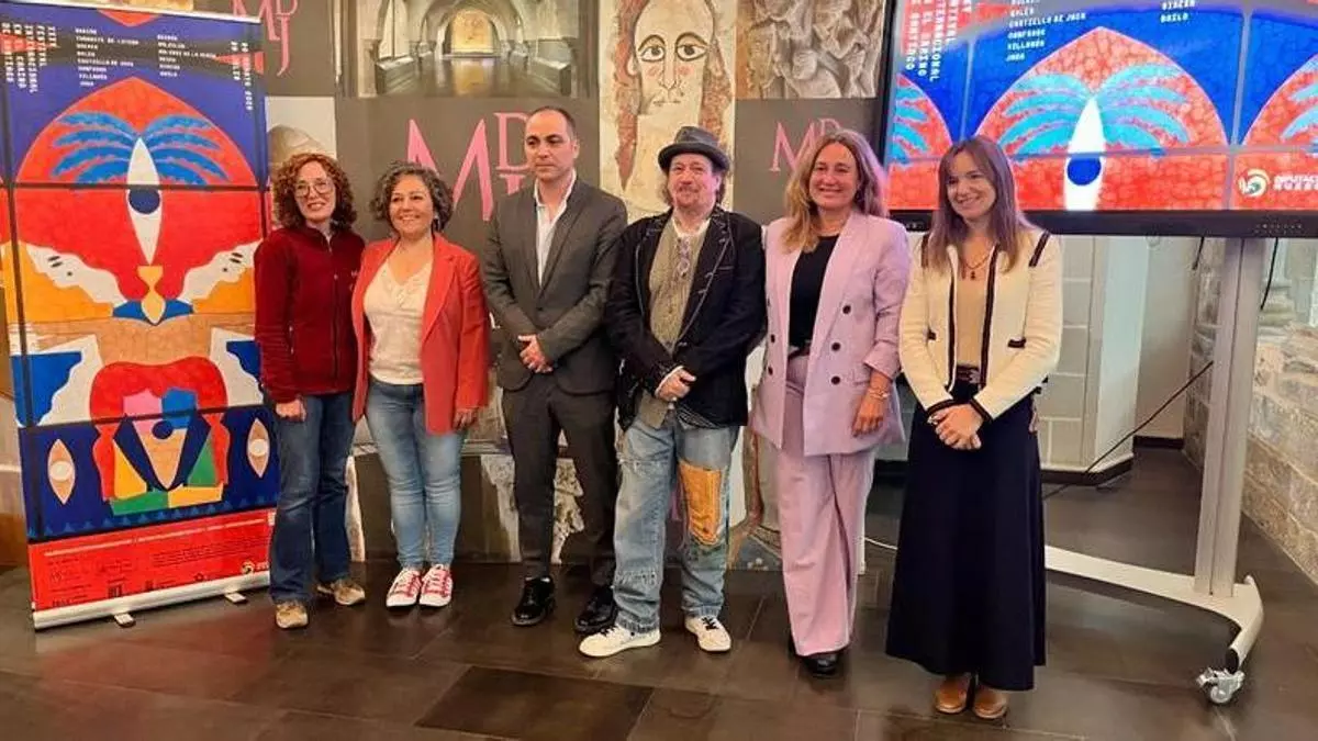 Six people pose for a photo in a gallery, standing beside vivid abstract artwork and two large digital screens.