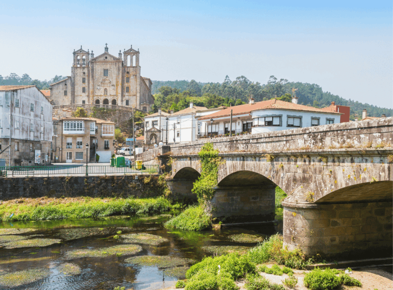 Stone bridge with arches over a river; historic town with a large church on a hill in the background.