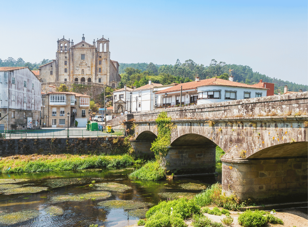 Stone bridge with arches over a river; historic town with a large church on a hill in the background.