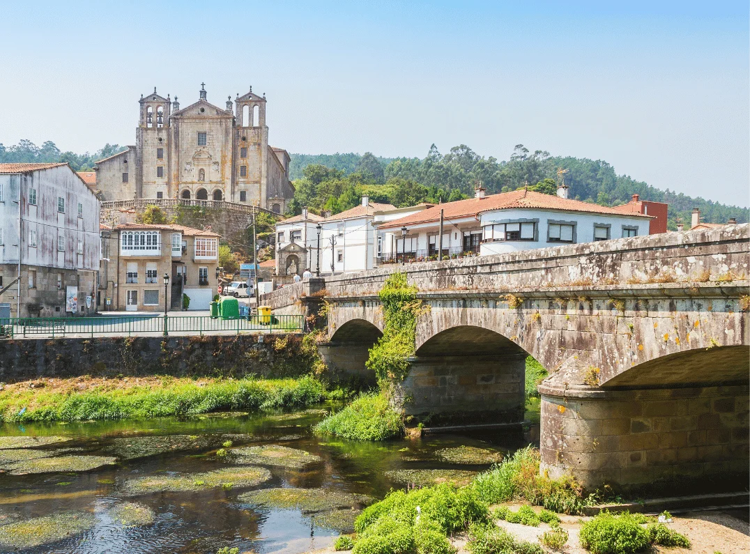Stone bridge with arches over a river; historic town with large church on hill in the background.