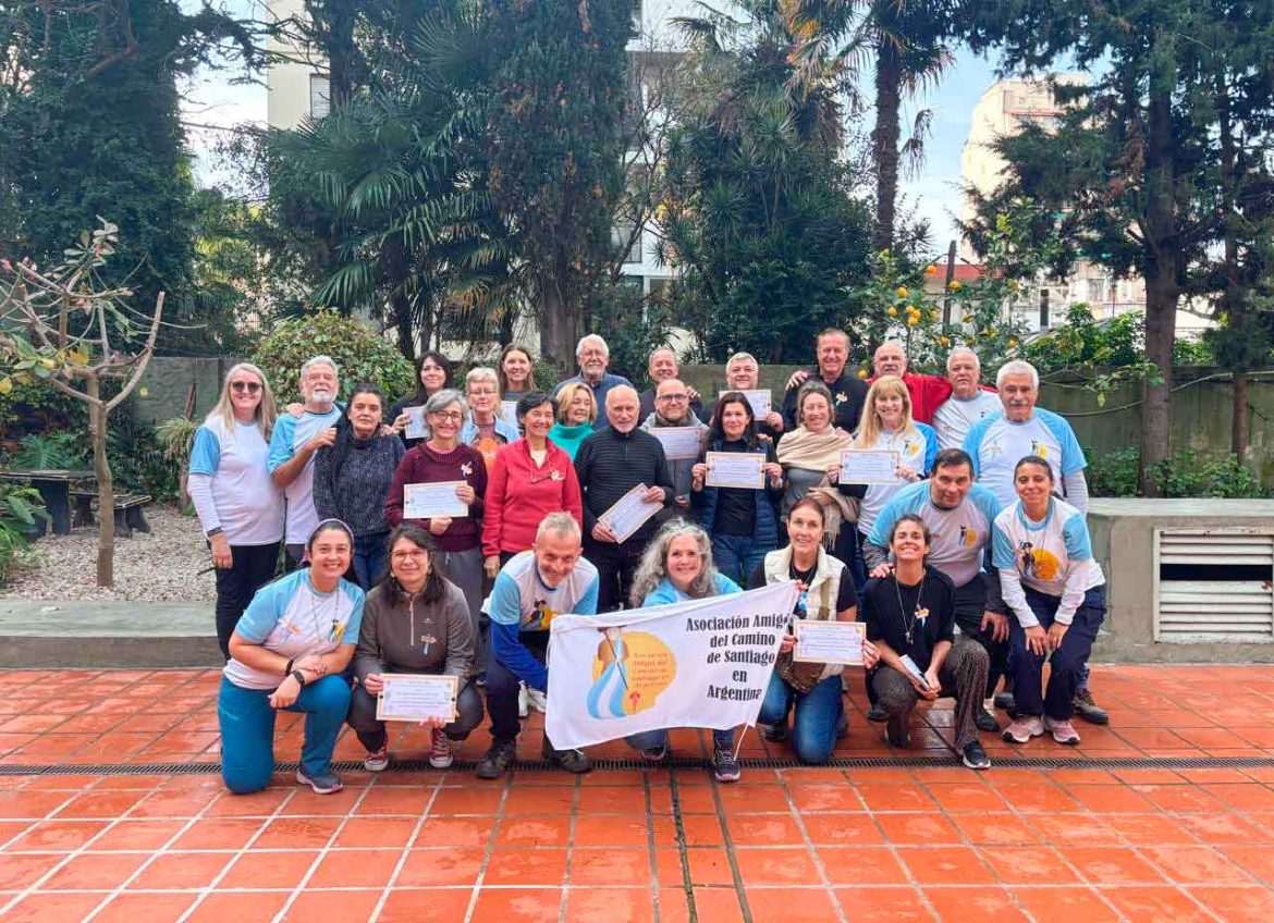 Group of diverse adults posing outdoors, holding certificates and a banner for the Asociación Amigos del Camino de Santiago en Argentina.
