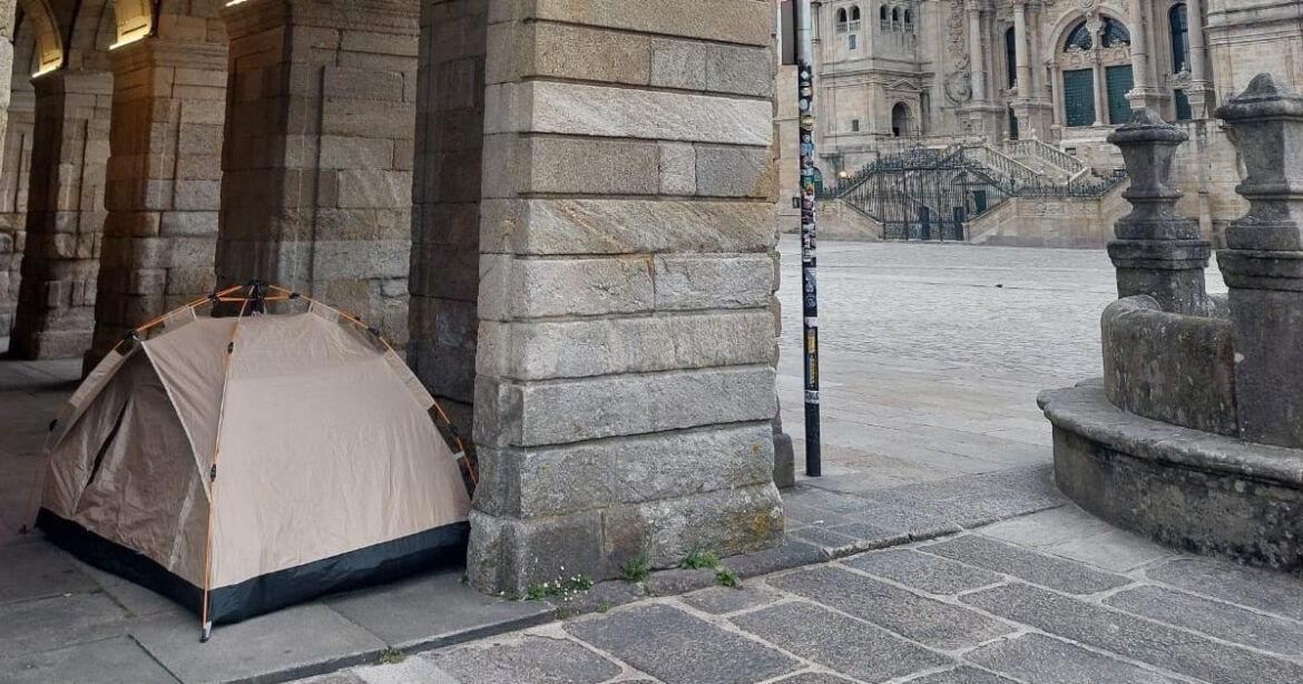 Beige camping tent pitched beside a stone archway in a historic plaza.