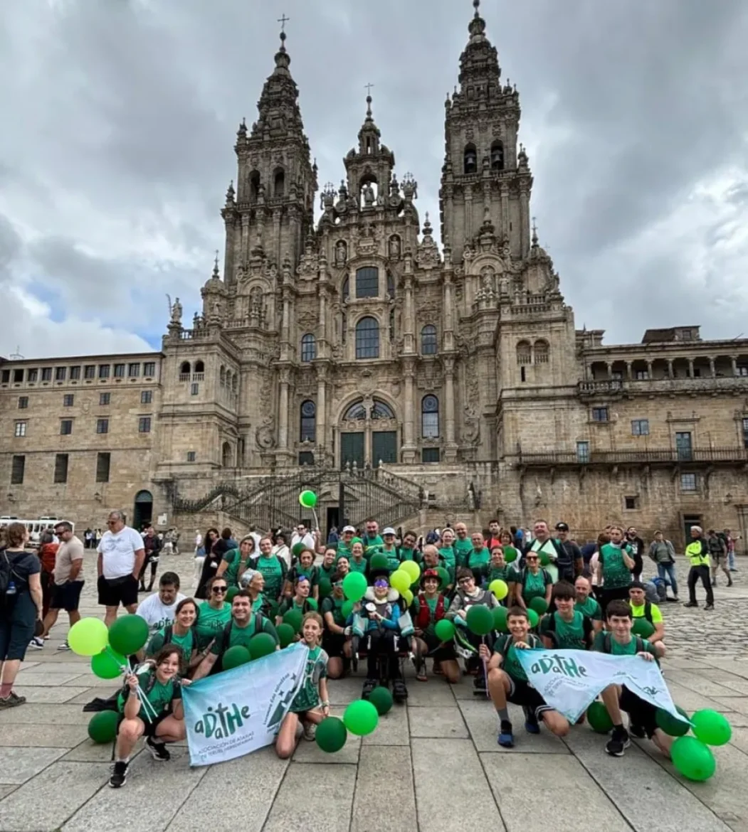 Group of people in green shirts posing with green balloons for a group photo in a plaza, in front of a grand ornate cathedral with tall spires and detailed stonework in the background.