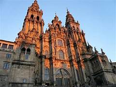 Sunlit, ornate cathedral facade with two tall towers set against a blue sky, showcasing detailed stone carvings and a grand entrance.