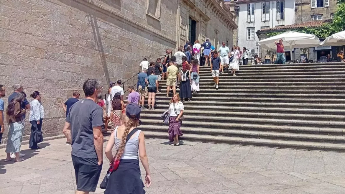 Crowd of people climbing a long stone staircase toward a historic building, with outdoor cafe umbrellas on the right.