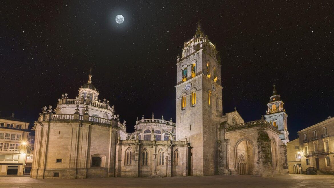 Moonlit historic cathedral complex with a tall clock tower in a quiet square, starry night sky and a visible moon above.