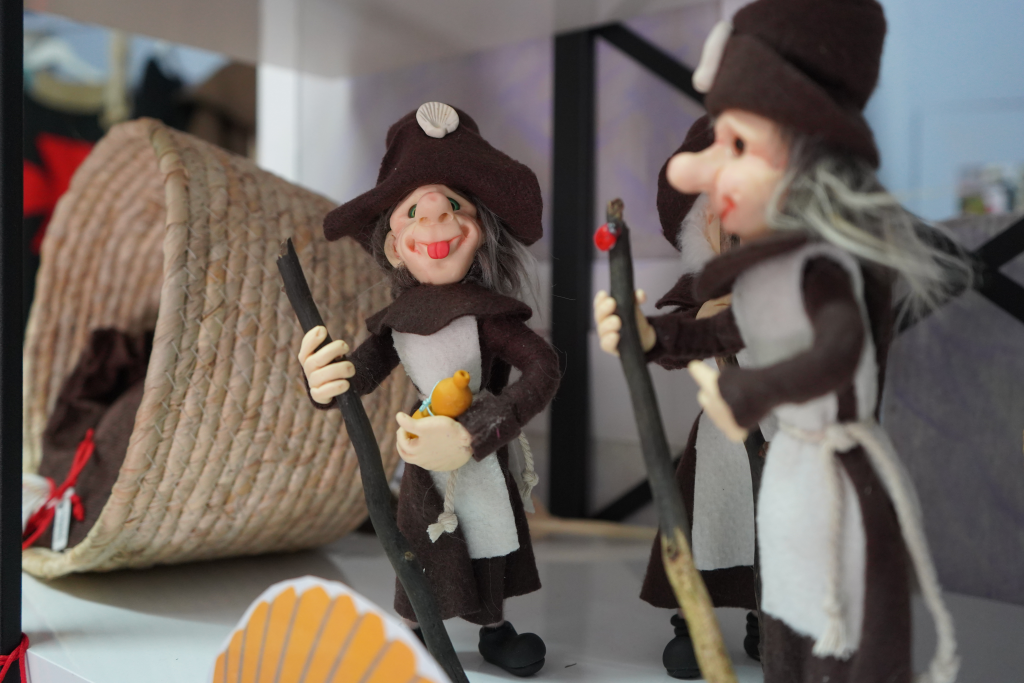 Two felt monk puppets in brown robes with walking sticks, one holding a yellow chick, on a display shelf.